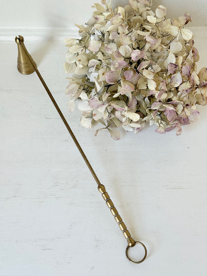 vintage brass candle snuffer with twisted handle and cone-shaped head photographed on white surface