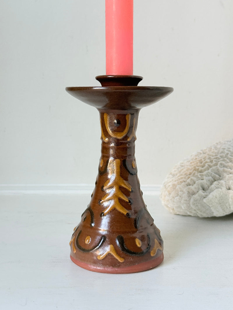 Vintage studio pottery candlestick in brown glaze with cut out decoration styled with coral taper candle on white surface