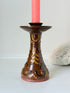 Vintage studio pottery candlestick in brown glaze with cut out decoration styled with coral taper candle on white surface