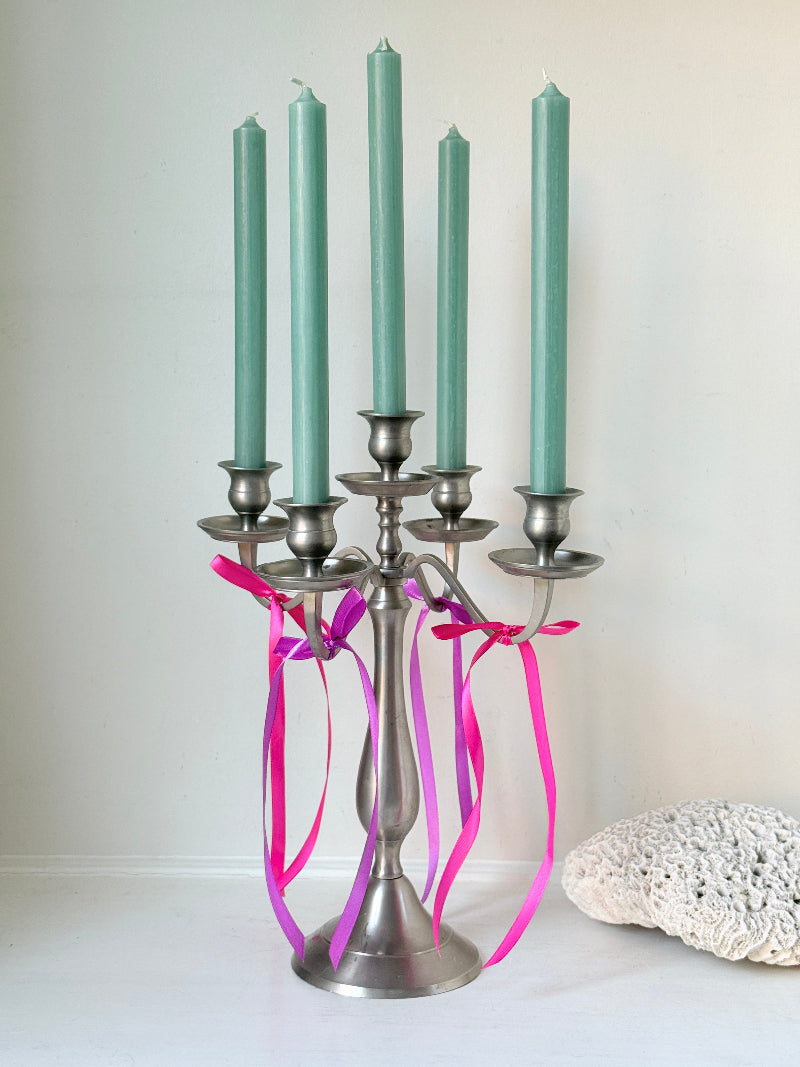 Five arm pewter style metal candelabra with aged silver finish styled with blue green taper candles on white surface