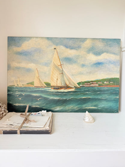 A vintage-style oil painting of sailboats on the blue ocean under a cloudy sky, displayed on a white shelf next to a wrapped book and a small shell.