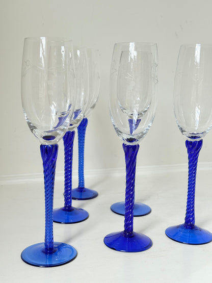 Set of six vintage French champagne flutes with tall clear bowls and cobalt blue twisted stems, photographed on white surface.