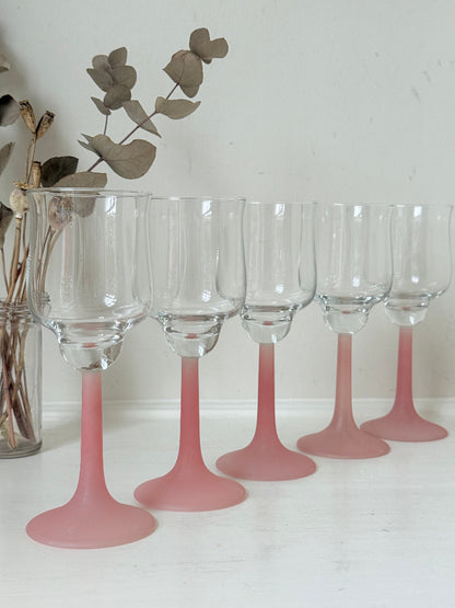 Set of five vintage wine glasses with clear bowls and pink stems photographed on a white surface.
