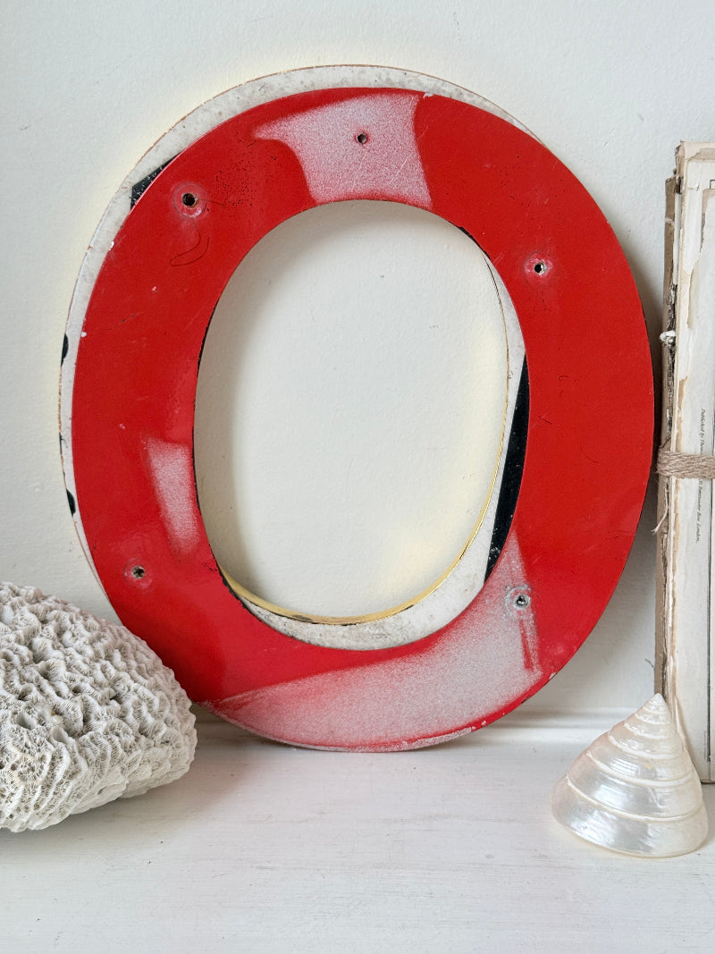 A rustic oval picture frame with a glossy red center and a distressed white outer border, styled with seashells on a white surface.
