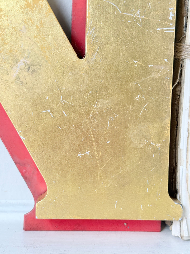 A close-up of a distressed gold decorative letter &
