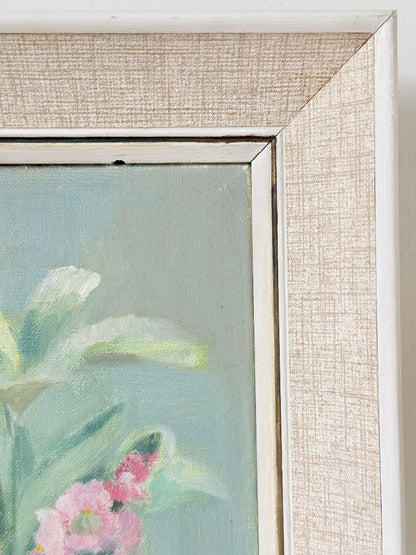 Close-up of a framed floral painting showing part of a pink flower with green leaves against a soft blue-green background, with a textured beige linen-like frame and white inner trim.
