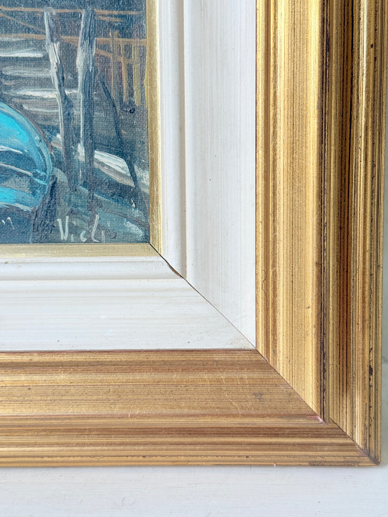 Close-up of a framed painting corner showing a distressed gold frame, white matting, and a blue-toned painted artwork.