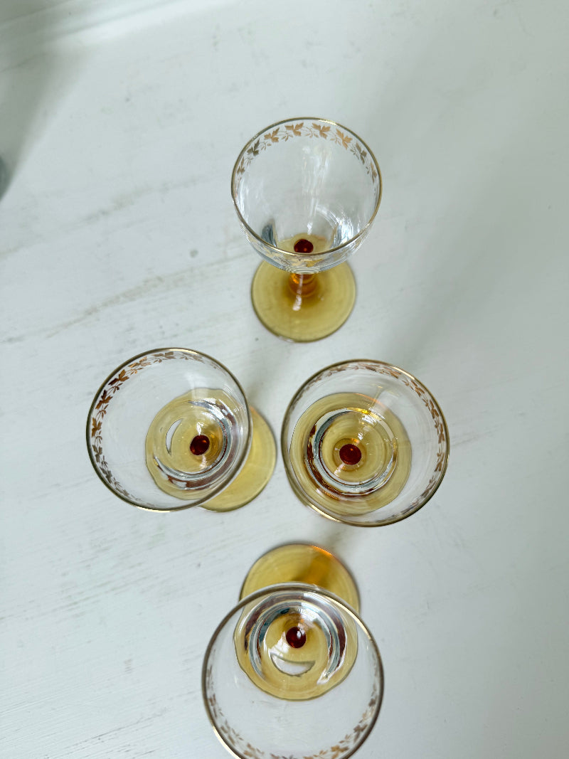 Vintage set of four shot glasses with amber stems and gilt rims, photographed on a white surface