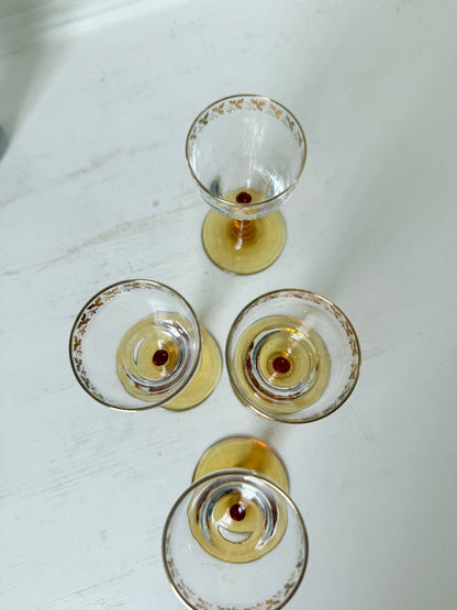 Vintage set of four shot glasses with amber stems and gilt rims, photographed on a white surface