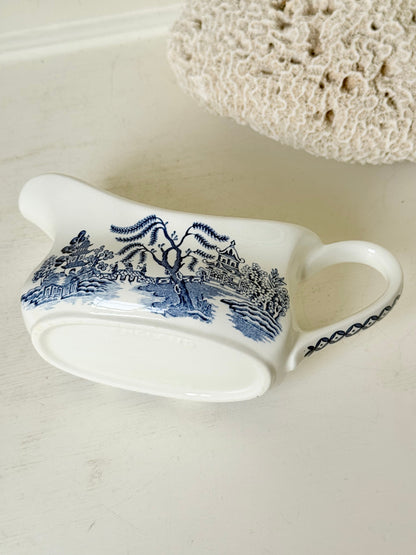 Vintage blue and white ceramic sauce boat with willow pattern photographed on a white surface
