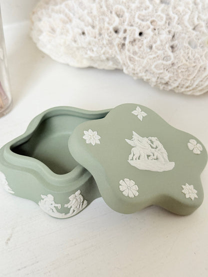 Vintage Wedgwood Jasperware sage green lidded trinket box in a quatrefoil shape, decorated with white neoclassical cherubs and florets, styled with dried stems.