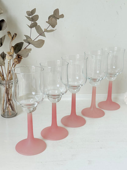 Set of five vintage wine glasses with clear bowls and pink stems photographed on a white surface.