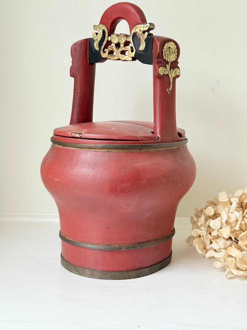 Vintage red painted wooden basket with upright handle and gold painted detail photographed on a white surface