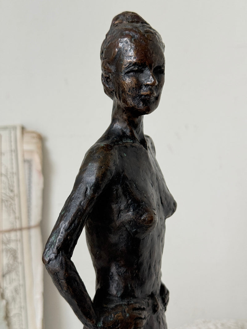 Solid bronze figure of a standing semi nude woman with upswept hair on a white marble base