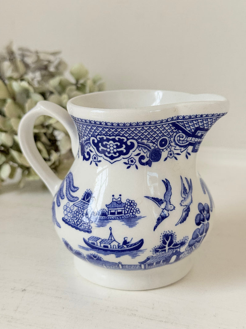 Vintage Churchill Blue Willow milk jug in blue and white ceramic photographed on a white surface.