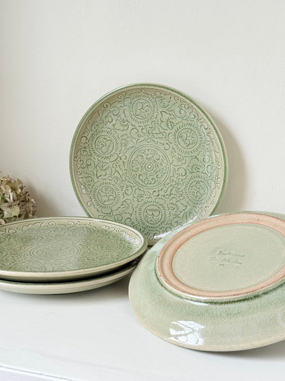 Set of four large Thai celadon stoneware plates in soft green glaze with raised pattern, photographed on a white surface