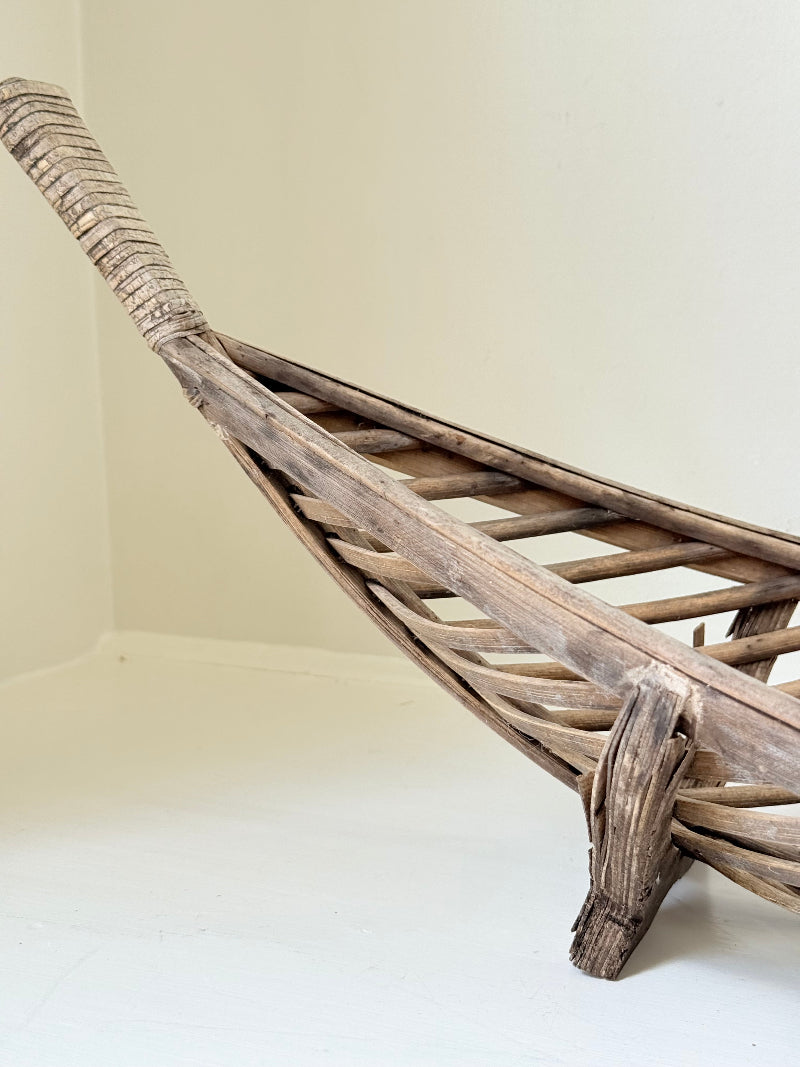 Large curved woven basket with slatted sides and repaired plywood base photographed on a white surface