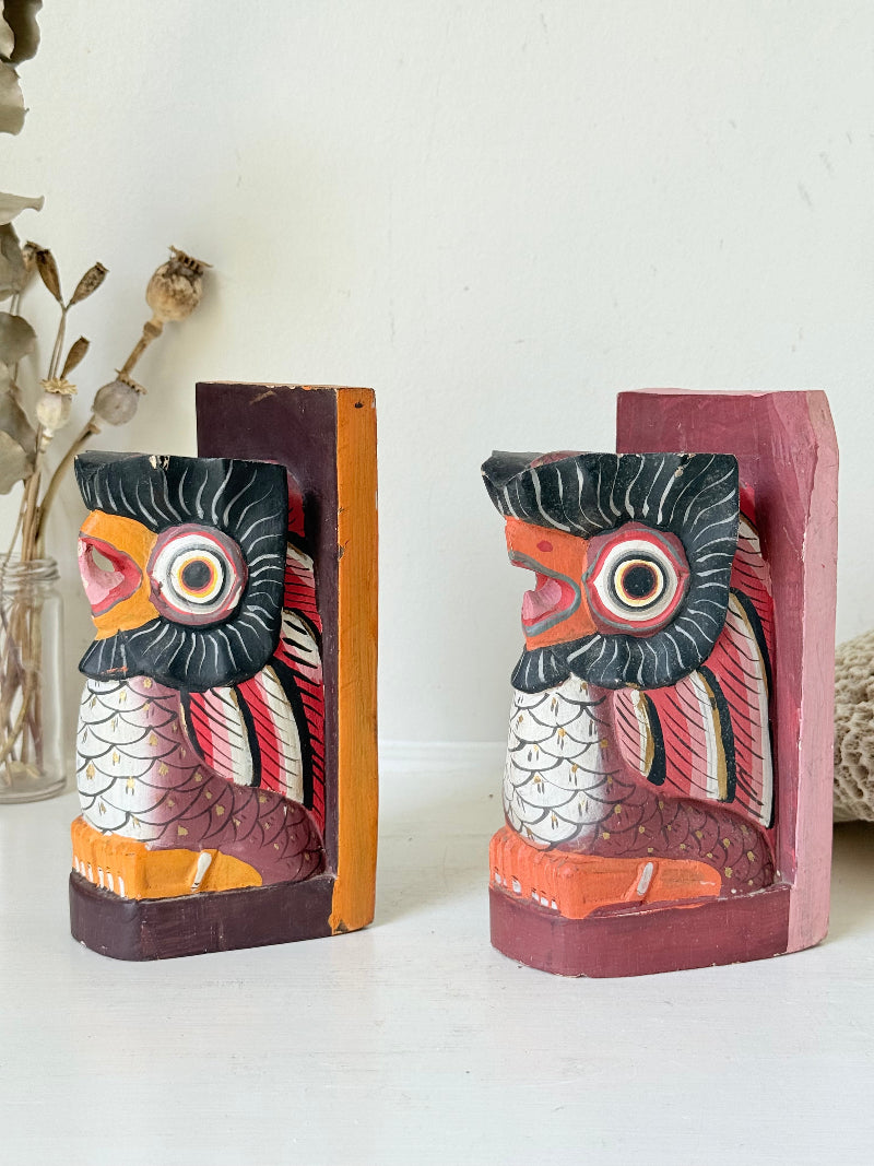 Vintage wooden owl bookends hand painted in red and orange tones, displayed on a white surface beside dried flowers.