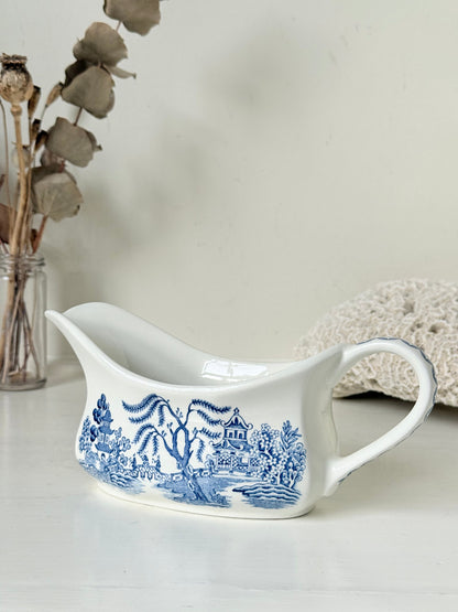 Vintage blue and white ceramic sauce boat with willow pattern photographed on a white surface