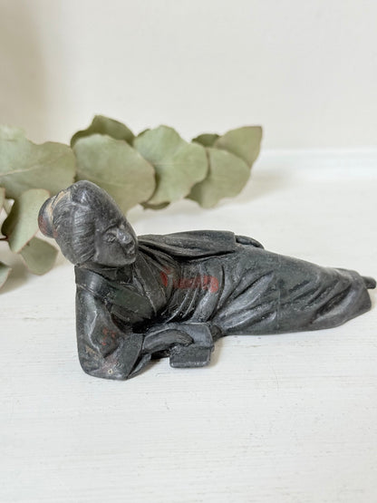 antique japanese bronze reclining lady with impressed marks to base photographed on white surface with foliage background