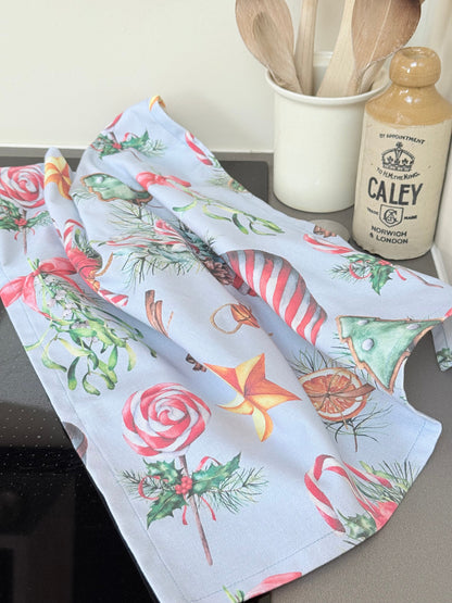 Blue Loft Christmas cotton tea towel with red striped stocking and festive motif pattern photographed on a white worktop.