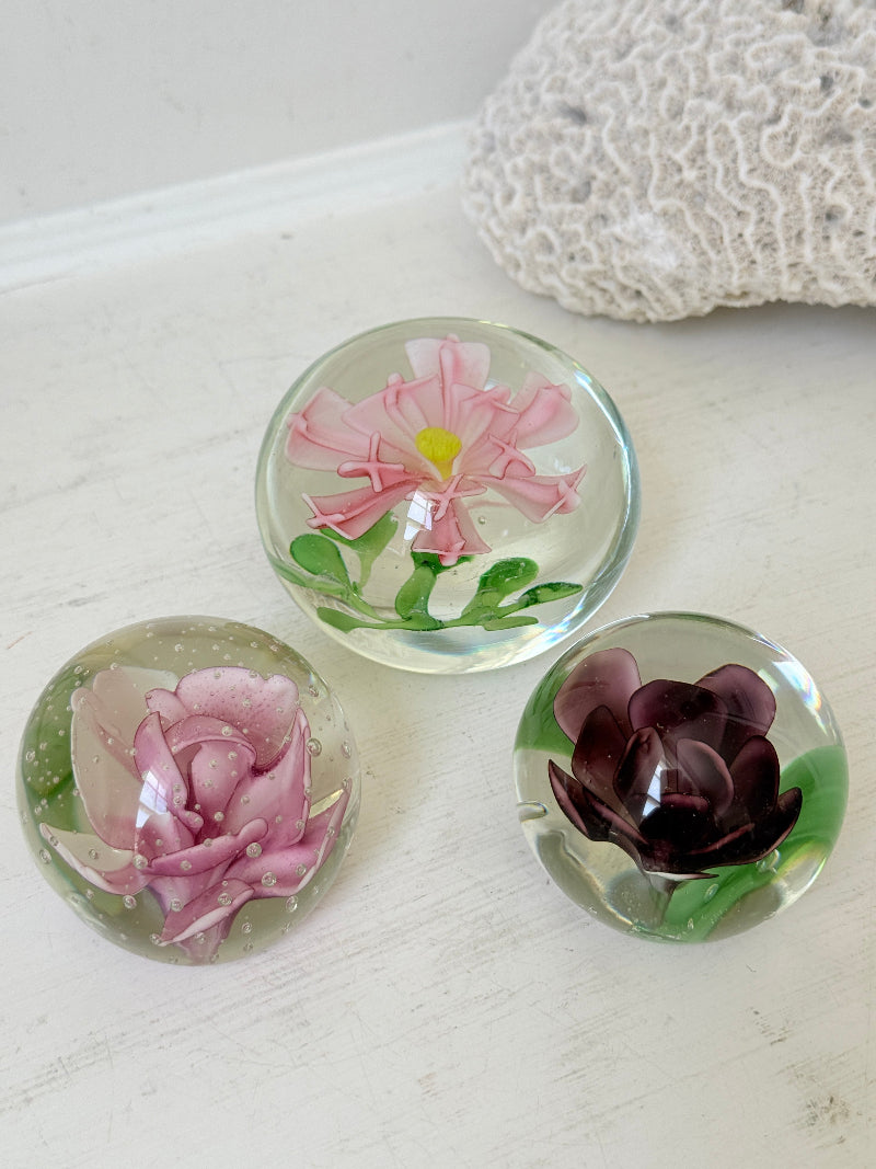 Trio of vintage glass paperweights with hand worked pink and plum floral detail, clear glass domes and green leaf decoration