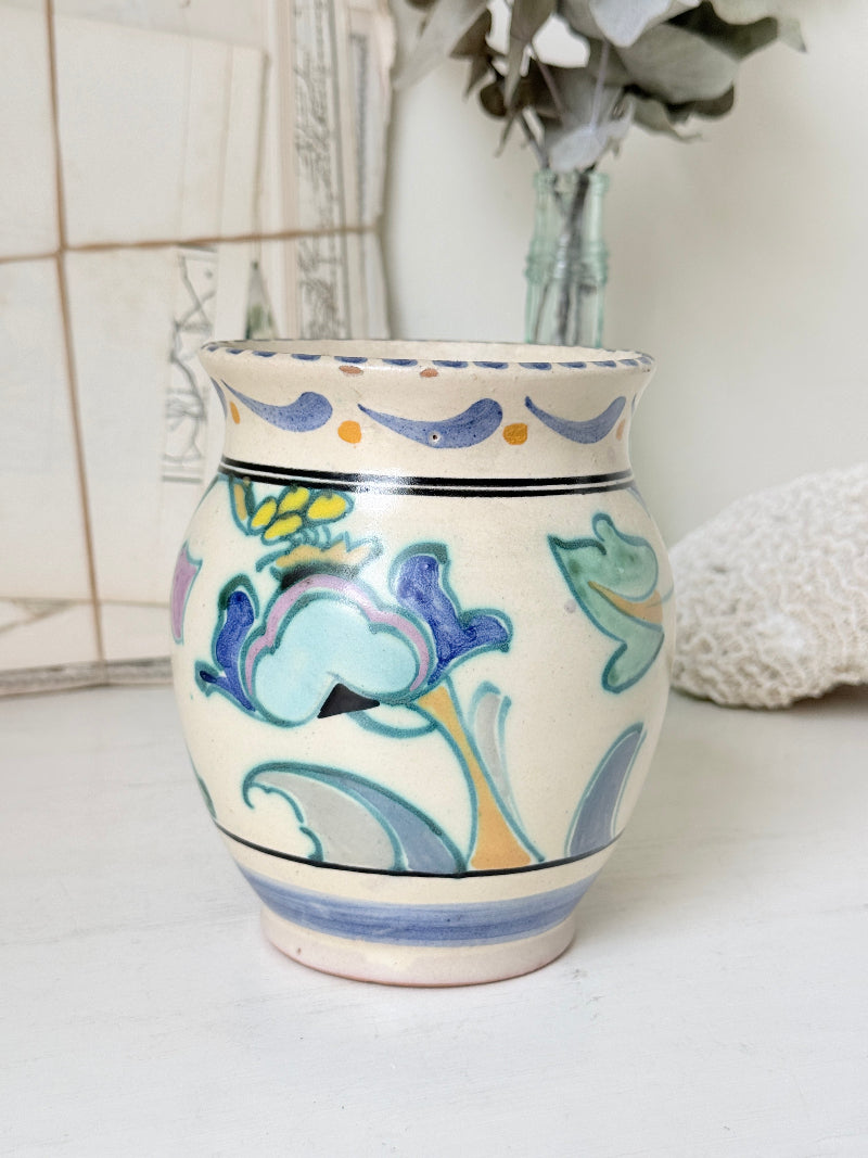 Hand painted floral pottery vase in blue and green on cream, photographed on a white surface
