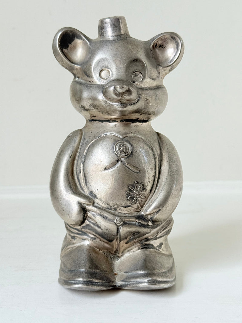 Vintage silver tone metal bear money box with coin slot on top, photographed on a white surface.