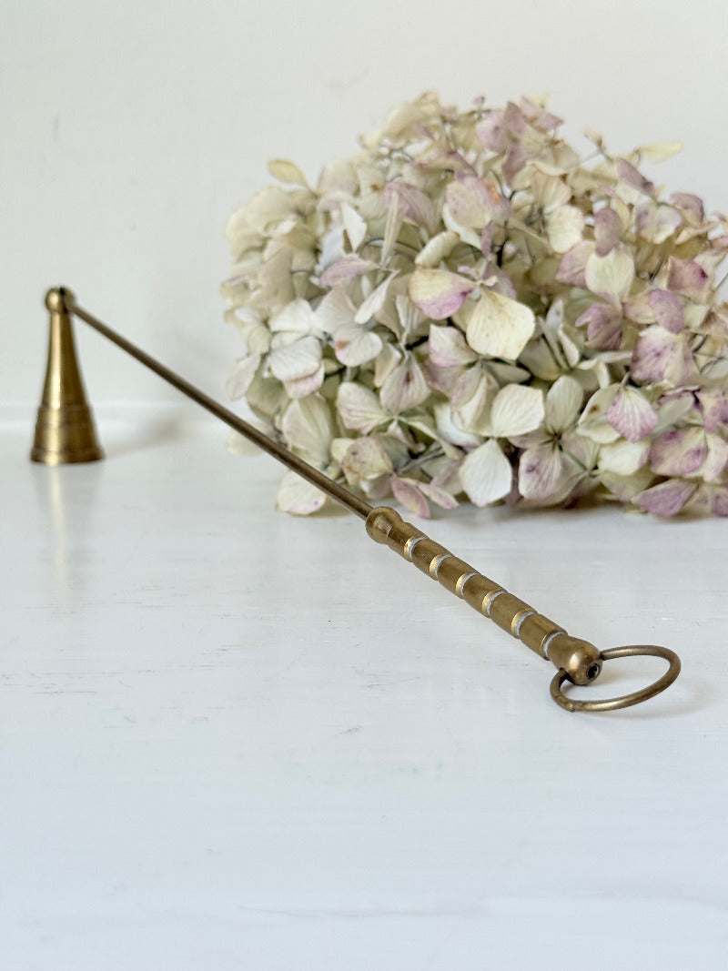 vintage brass candle snuffer with twisted handle and cone-shaped head photographed on white surface