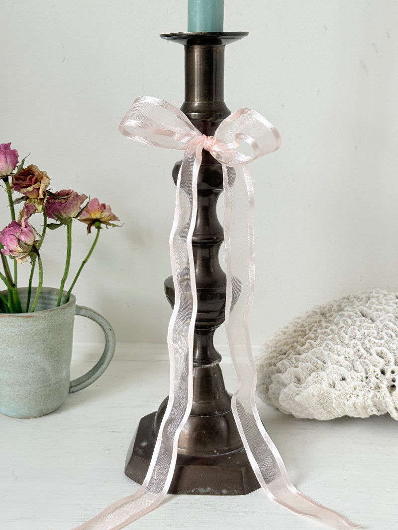 Bronze coloured vintage candlestick with bobbin stem and shaped base styled with taper candle on white surface
