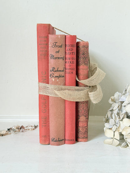 A decorative arrangement of five vintage-style red and pink book spines tied together with a natural jute ribbon. Visible titles include Frost at Morning, and How to Make to Propose Them.