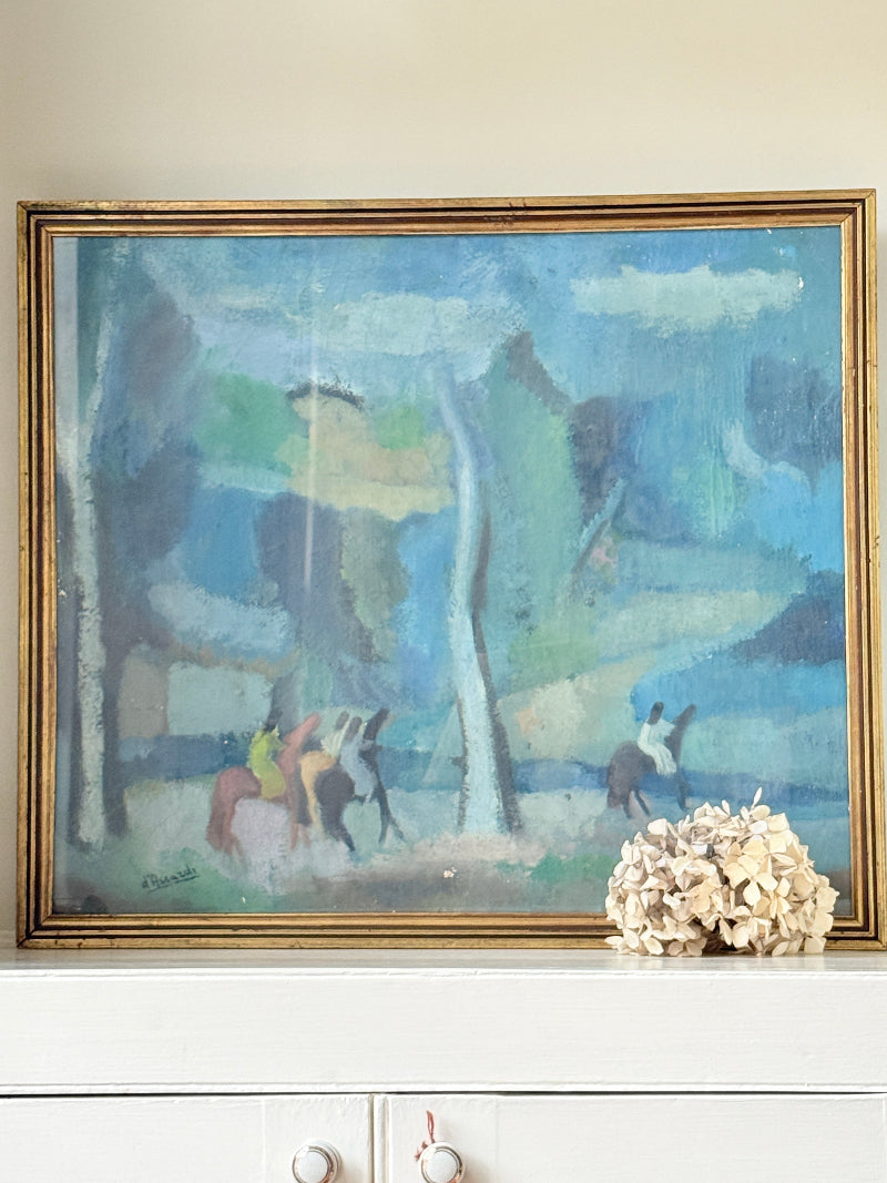 A framed impressionist landscape painting featuring blue, green, and gray tones with horse riders, displayed on a white mantelpiece next to a dried floral arrangement.