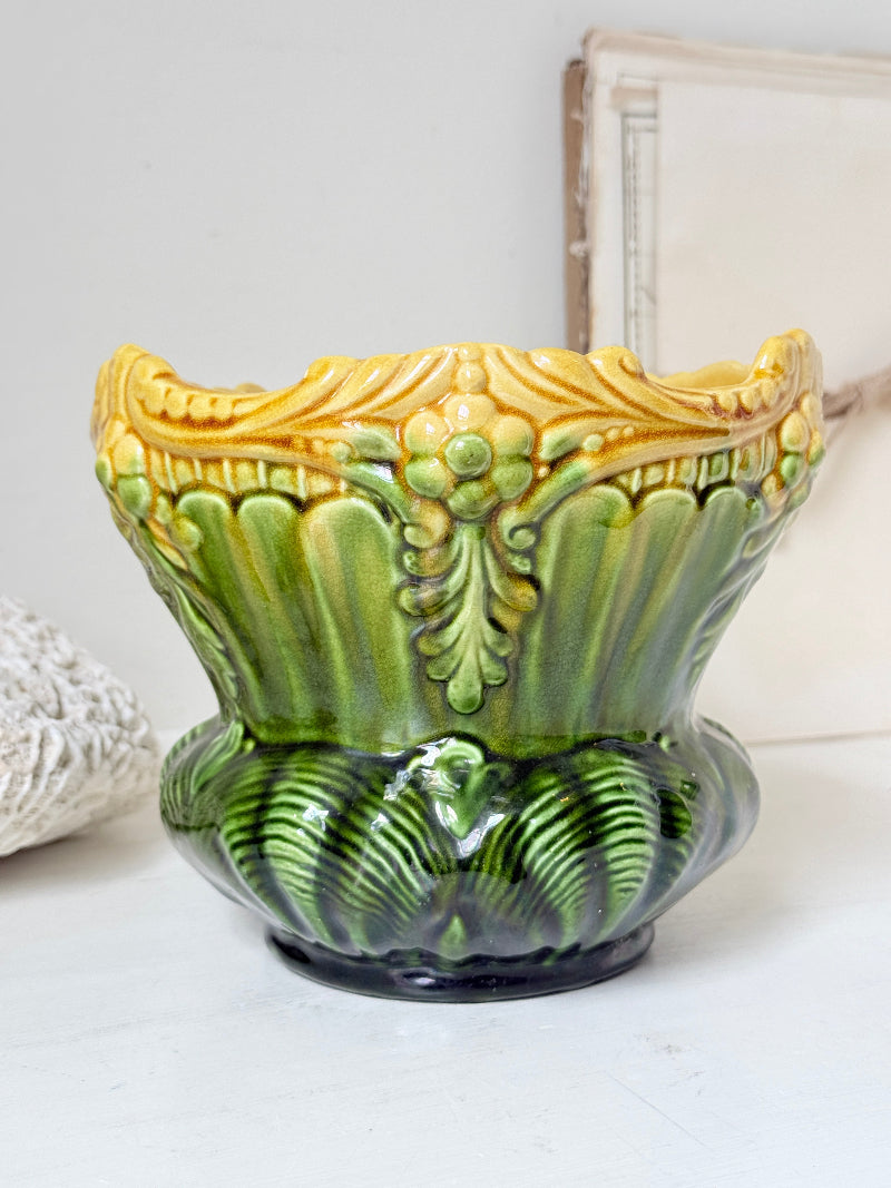 A vintage ceramic planter pot with a green and yellow glaze, featuring a fluted leaf-like design and a scalloped rim, set against a neutral background.