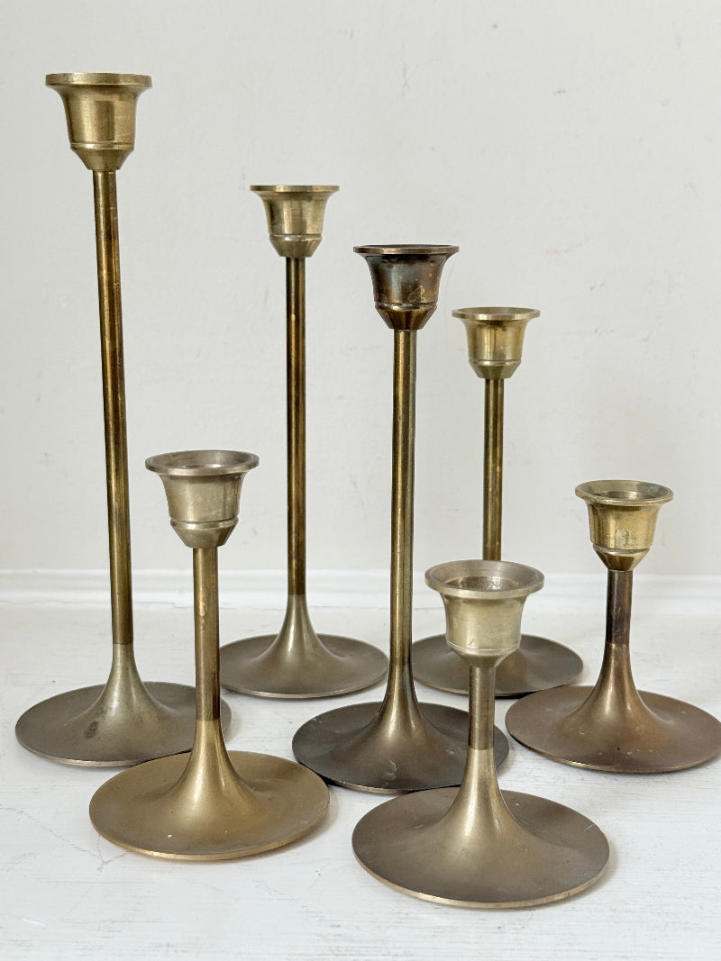 Set of 7 vintage brass candlesticks in graduated heights with aged brass finish styled with red ribbon on white surface