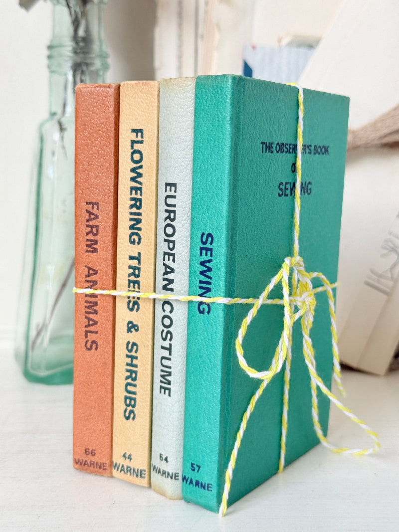 Four decorative hardcover books tied together with yellow-and-white twine, standing upright on a light surface. The spines read &