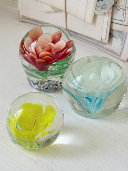 Trio of vintage glass paperweights with red flower, yellow flower and turquoise swirl decoration in clear coloured glass