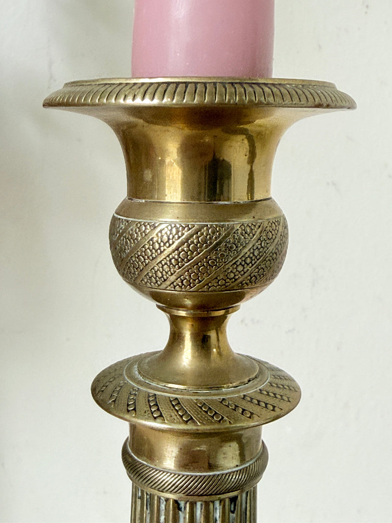 Pair of antique brass Empire style candlesticks photographed on a white surface with fluted columns and circular bases holding pink taper candles