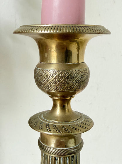 Pair of antique brass Empire style candlesticks photographed on a white surface with fluted columns and circular bases holding pink taper candles