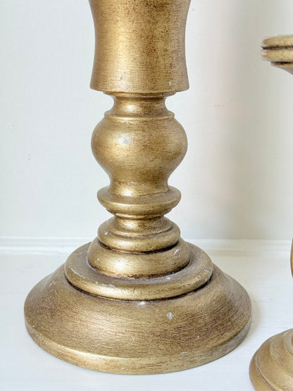 Pair of vintage wooden candlesticks, one tall and one small, in golden-toned finish, styled with pillar candles on a white surface.