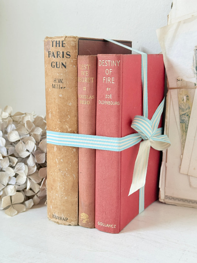 Three antique red books with aged spines tied with a turquoise striped ribbon on a white surface, styled with glass and beads