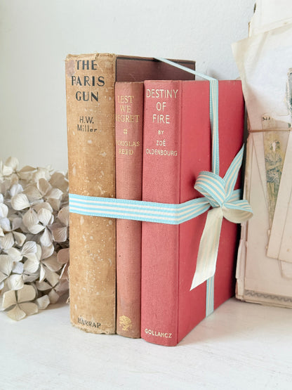 Three antique red books with aged spines tied with a turquoise striped ribbon on a white surface, styled with glass and beads