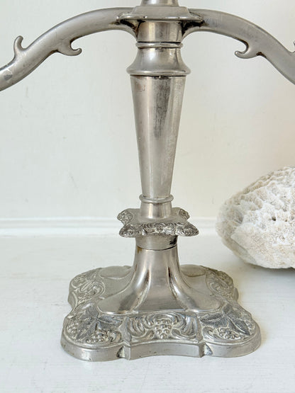 Vintage silver coloured three-arm candelabra with ornate base and soft patina, photographed on a white surface