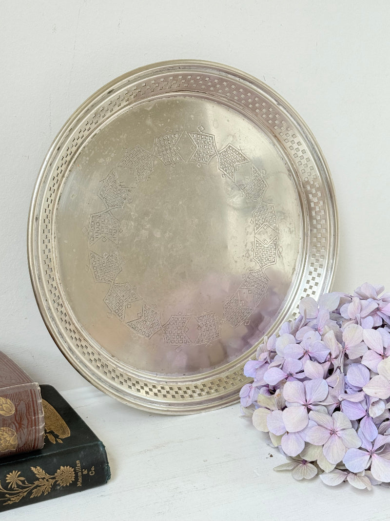 Vintage round silver plate tray with brass rim, pierced edge and etched central motif, photographed on white surface