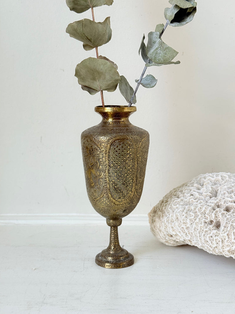 Indian Benares brass chalice vase with figural panels and pedestal base, photographed on a white surface