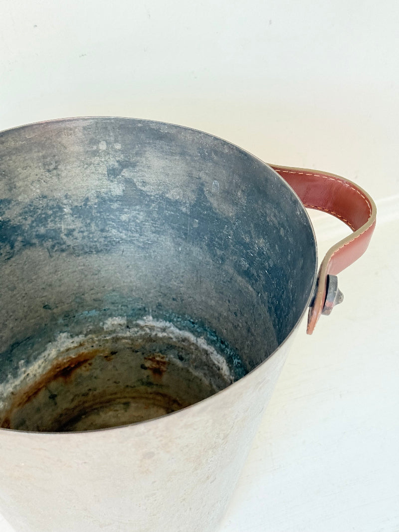 Vintage metal wine cooler with leather handles and tapered form, photographed on white surface.