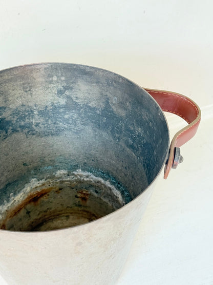Vintage metal wine cooler with leather handles and tapered form, photographed on white surface.