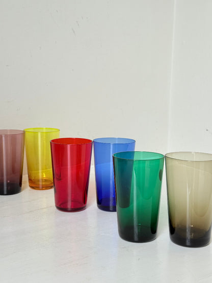 Set of six mid-20th century Boussu coloured glass beakers in rainbow hues, green with original label, photographed on white surface.
