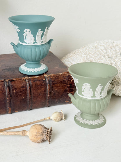 Pair of vintage Wedgwood Jasperware pedestal urns in sage green and pale blue, decorated with white neoclassical figures, styled on an antique leather book.