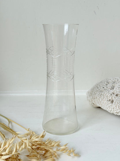 Vintage clear glass cylinder vase with etched leaf design, photographed on a white surface.