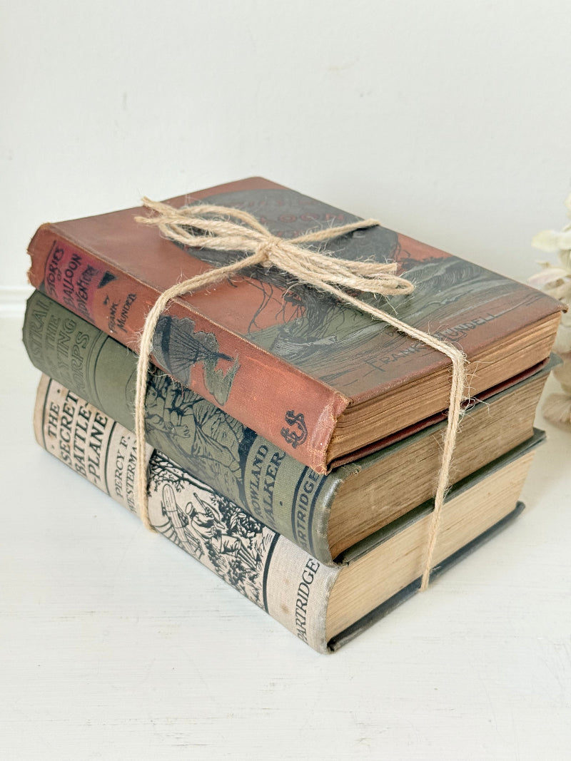 Vintage decorative book bundle in red, olive green and cream tied with twine, photographed on a white surface